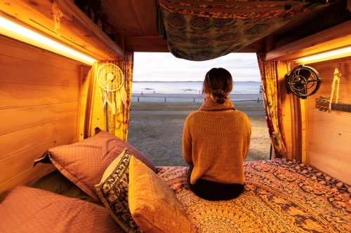 Woman watching sunset over beach from bohemian camper van in a van life theme