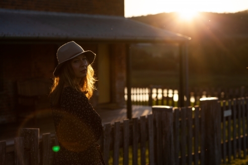 Woman wearing a hat next to a farmhouse during late afternoon - Australian Stock Image