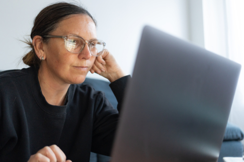 Woman wearing black jumper with eyeglasses working on laptop at home - Australian Stock Image