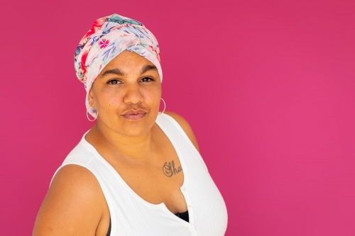 woman wearing floral head wrap in front of magenta background - Australian Stock Image