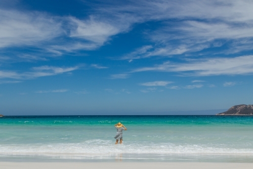 Woman wearing straw hat wading into the blue ocean