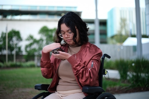 Woman with a disability sitting in a wheelchair looking down at her mobile phone
