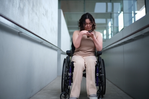 woman with a disability sitting in a wheelchair looking down at her mobile phone - Australian Stock Image