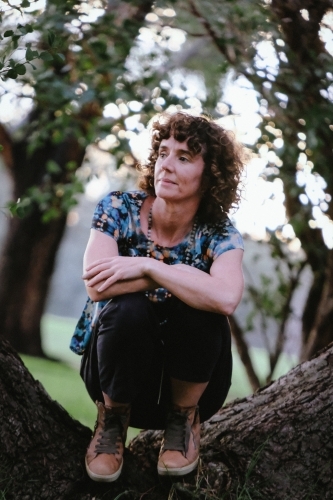 woman with curly hair and casually dressed sitting on tree trunk - Australian Stock Image