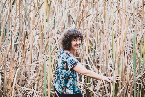 Woman with curly hair posing in front of bushland and reeds grass - Australian Stock Image
