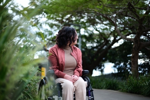Woman with disability sitting in a wheelchair outside next to a tall grass - Australian Stock Image