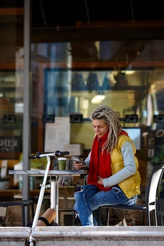 Woman with dreadlocks at cafe with mobile phone and electric scooter - Australian Stock Image