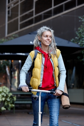 Woman with dreadlocks on electric scooter going to her yoga class - Australian Stock Image