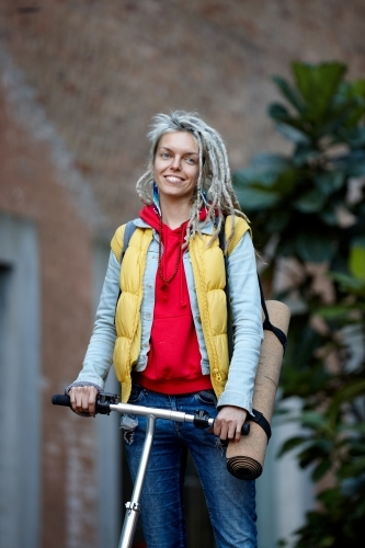 Woman with dreadlocks on electric scooter going to yoga class - Australian Stock Image