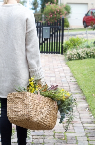 Woman with market basket of wild flowers walking along footpath - Australian Stock Image