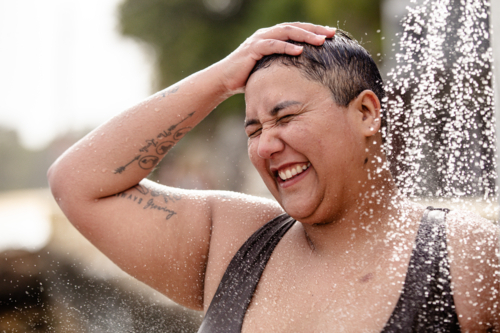 Woman with tattoos standing under an outdoor shower - Australian Stock Image