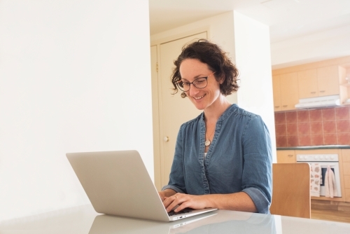 Woman working on laptop in dining area looking at computer. - Australian Stock Image