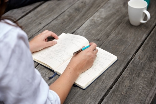 Woman writing on notepad on wooden table outdoors