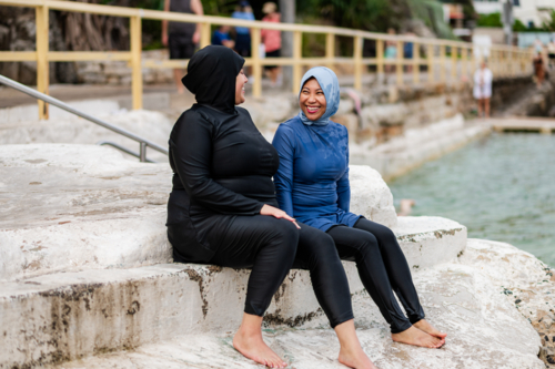 Women in burkinis sitting on the platform of ocean pool - Australian Stock Image