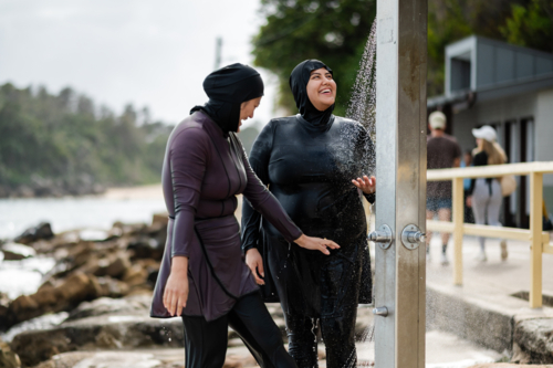 Women in burkinis under the pouring water from the beach shower near ocean pool - Australian Stock Image