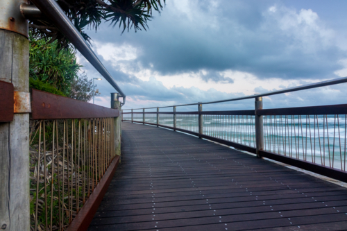 Wooden boardwalk curving around coastline with ocean and clouds - Australian Stock Image