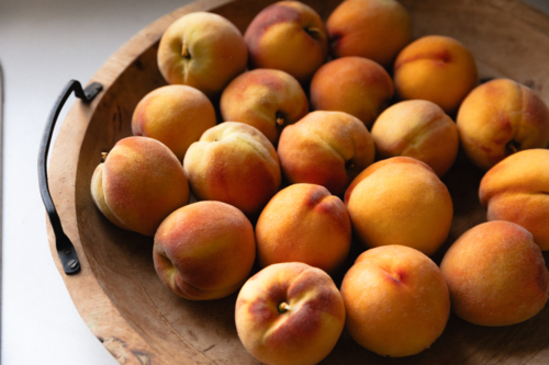 Wooden bowl full of freshly picked ripe peaches on kitchen bench in natural window light - Australian Stock Image