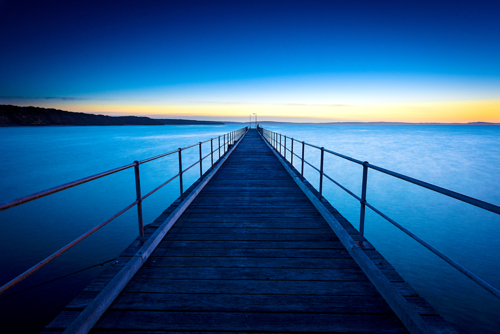 Wooden pier stretching into the calm sea at dawn - Australian Stock Image