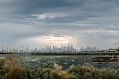 Wooden pier stretching toward city skyline under cloudy sky - Australian Stock Image