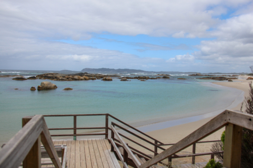 Wooden stairs down to a beach with large boulders on a cloudy day - Australian Stock Image