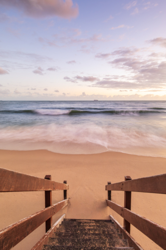 Wooden stairs leading to beach at sunset with waves breaking - Australian Stock Image
