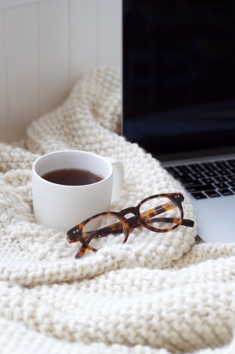 Woollen knitted blanket with coffee mug, glasses and laptop computer - Australian Stock Image
