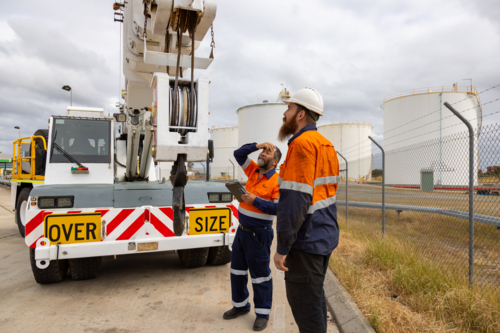 workers looking at the top of pick and carry franna crane truck on industrial site - Australian Stock Image