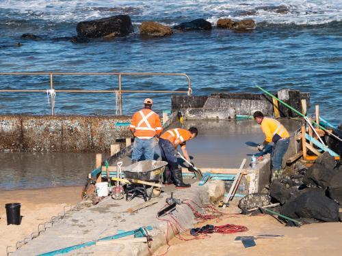 Workmen concreting a seaside swimming pool wall - Australian Stock Image