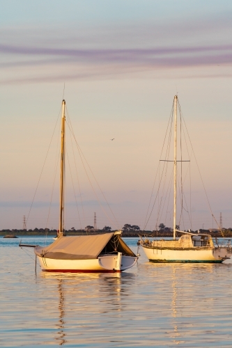 Yachts and their reflections on calm water in late afternoon light.