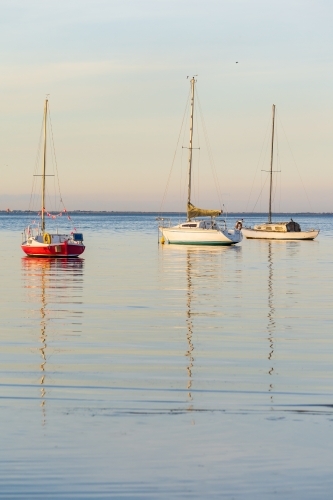 Yachts and their reflections on calm water in late afternoon light. - Australian Stock Image