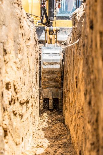 Yellow excavator digging trench with toothed trenching bucket - Australian Stock Image