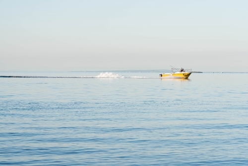 yellow fishing boat cruising along the calm  blue bay