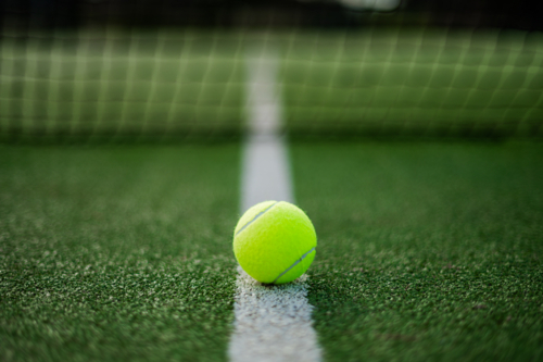Yellow tennis ball rests on white line of artificial grass court before tennis match - Australian Stock Image