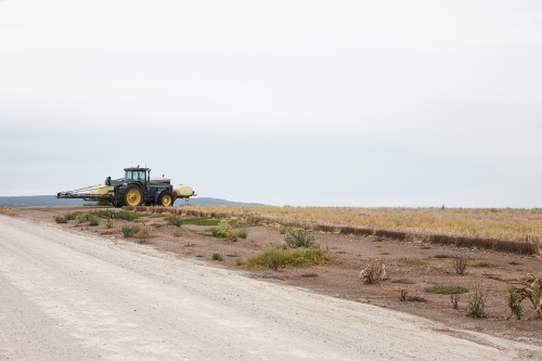 yellow tractor in an empty field and road - Australian Stock Image
