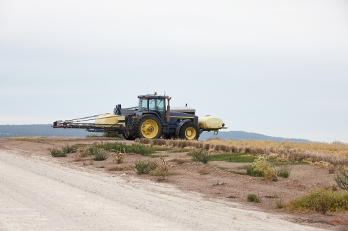 yellow tractor in an empty field and road - Australian Stock Image