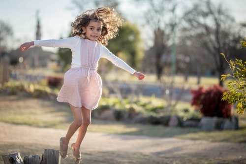 Young aboriginal and caucasian mixed race girl jumping off tree stump in garden - Australian Stock Image