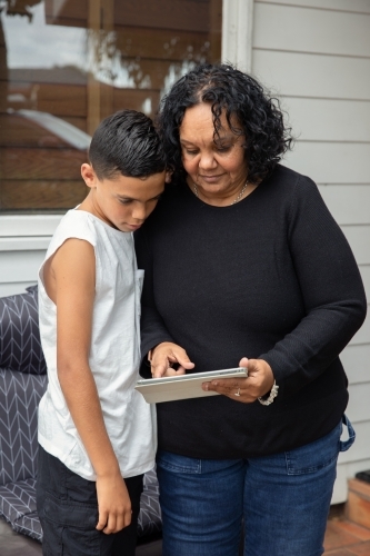 Young Aboriginal boy and Aboriginal woman looking at a device outside - Australian Stock Image