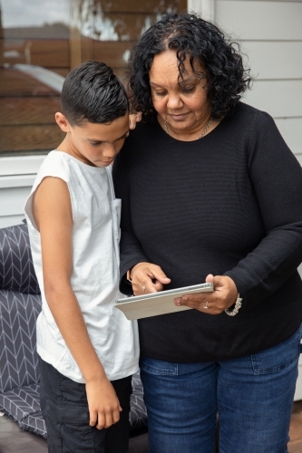 Young Aboriginal boy and Aboriginal woman looking at a device outside - Australian Stock Image