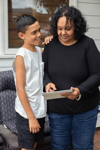 Young Aboriginal boy and Aboriginal woman looking at a device outside - Australian Stock Image