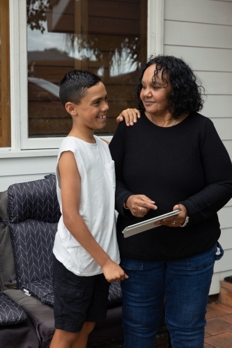 Young Aboriginal boy and Aboriginal woman looking at a device outside - Australian Stock Image