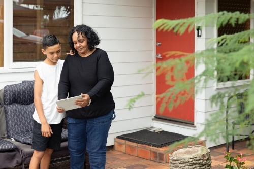 Young Aboriginal boy and Aboriginal woman looking at a device outside - Australian Stock Image