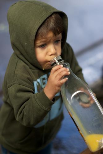 Young Aboriginal Boy in Green Top Drinking From Large Juice Bottle - Australian Stock Image