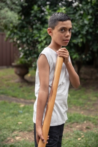 Young Aboriginal boy playing a didgeridoo in the backyard - Australian Stock Image