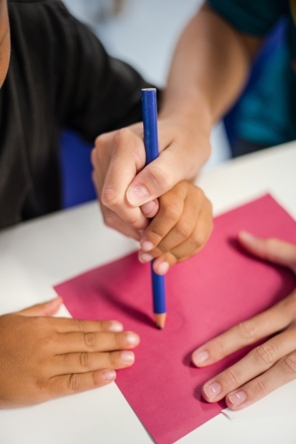 Young Aboriginal boy writing with teacher - Australian Stock Image