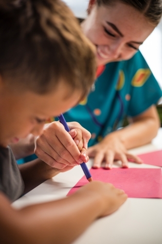 Young Aboriginal boy writing with teacher - Australian Stock Image