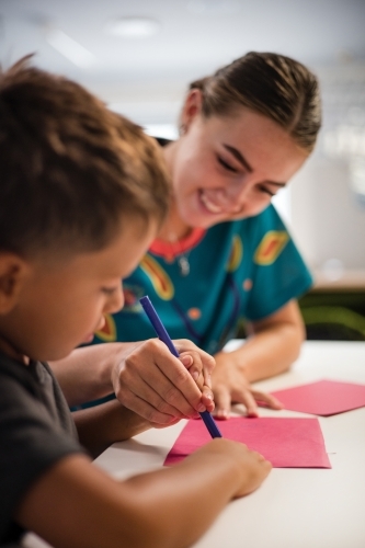 Young Aboriginal boy writing with teacher - Australian Stock Image
