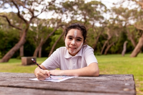 Young Aboriginal girl sitting at table drawing and smiling at the camera - Australian Stock Image