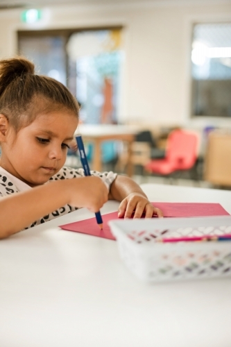Young Aboriginal girl writing at preschool - Australian Stock Image