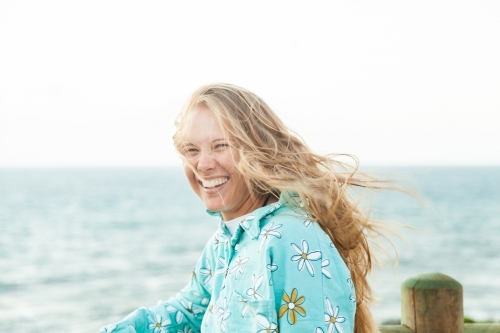 Young adult looking out over the ocean laughing with wind blowing her hair - Australian Stock Image