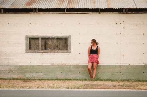 Young adult woman leaning against old building in remote farming community - Australian Stock Image